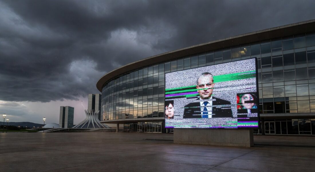 Edifício da CLDF em Brasília com tela de transmissão ao vivo com falhas, representando ineficiência e frustração dos cidadãos do DF.