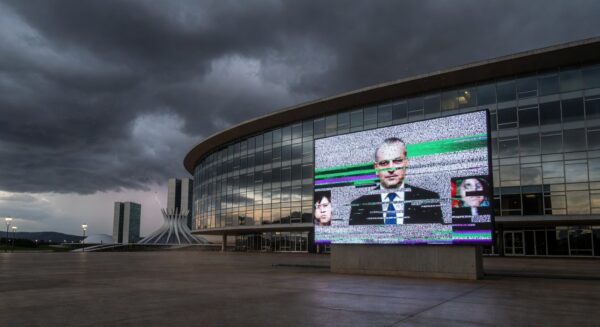 Edifício da CLDF em Brasília com tela de transmissão ao vivo com falhas, representando ineficiência e frustração dos cidadãos do DF.