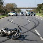 Cena de acidente na Epia em Brasília com moto danificada e viaturas policiais, representando tragédia com motociclista.