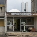 Hospital público em Brasília com fachada deteriorada e ambulâncias antigas, destacando falhas crônicas na saúde pública.