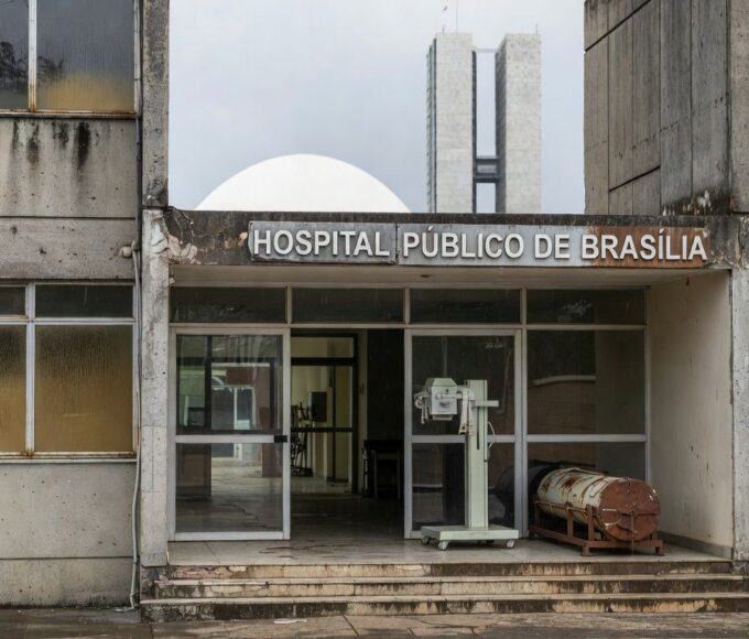 Hospital público em Brasília com fachada deteriorada e ambulâncias antigas, destacando falhas crônicas na saúde pública.