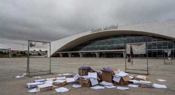 Edifício da Câmara Legislativa do DF em Brasília, com símbolos de homenagem e crises ignoradas, sob céu nublado.