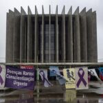 Banner com listras de zebra no prédio da CLDF em Brasília, destacando falhas no sistema de saúde para doenças raras.