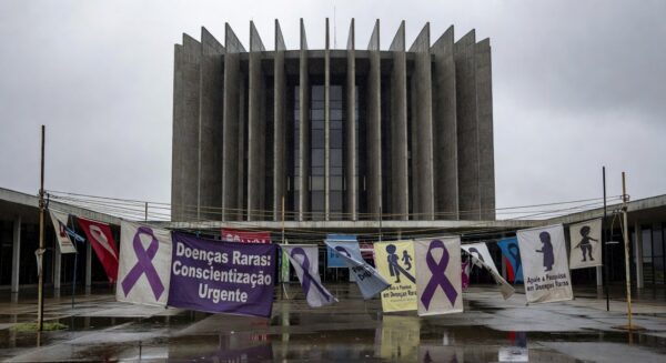 Banner com listras de zebra no prédio da CLDF em Brasília, destacando falhas no sistema de saúde para doenças raras.