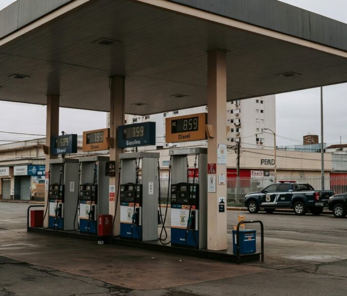 Posto de gasolina no Brasil com preços altos de combustíveis e viaturas da Polícia Federal, ilustrando investigação de aumentos abusivos.