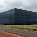 Sede da Caesb em Brasília com bandeira a meio mastro sob céu nublado, representando luto pelo falecimento de Marcelo Reis.