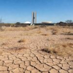 Paisagem seca em Brasília com solo rachado e vegetação murcha, destacando a seca e resposta tardia da Caesb com pontos de hidratação.
