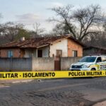 Casa isolada por fita de cena de crime em Águas Lindas de Goiás, com viatura da Polícia Militar, simbolizando tragédia familiar.